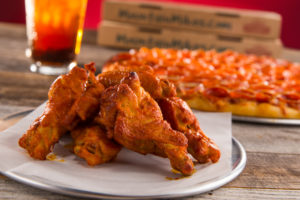 db&m Media Food Photography Services. Close-up of chicken wings with pizza in the background